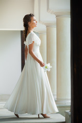 Young elegant woman with wedding bouquet in a light long white dress  before ceremony