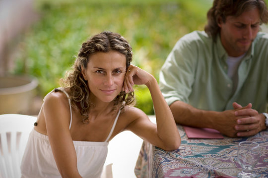 A beautiful woman is sitting while a man is seen in the background.