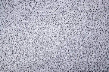 Morning pattern of chaotically arranged drops of water passed the day before rain or dew on the metal front hood of a bluish gray car.