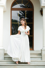 Fototapeta premium Beautiful young woman walking in long white dress. Tender bride with wedding bouquet.