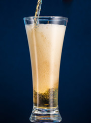 Full narrow glass of beer with foam on a blue background