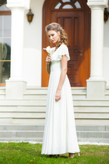 Fototapeta premium Beautiful young woman walking in long white dress. Tender bride with wedding bouquet.