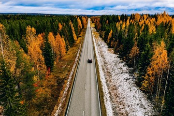 Aerial view of first snow autumn color forest and a road with car in Finland.