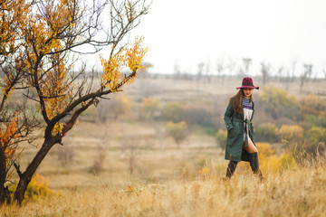 Beautiful young stylish girl in a coat walks in the autumn in the park. The girl is dressed in a green coat and a red hat. Beautiful evening. Autumn fashion. Lifestyle. High fashion portrait. 