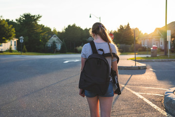 Teen girl depressed/sad at sunset in a parking lot while wearing a backpack and holding binders.