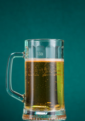 Glass of beer with foam and spray from falling ice on a turquoise green background