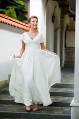 Beautiful young woman walking in long white dress. Tender bride with wedding bouquet.