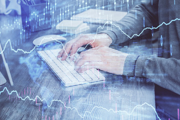 Double exposure of man's hands writing notes with laptop of stock market with forex graph...