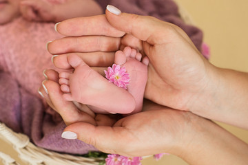 Obraz na płótnie Canvas Feet of the newborn baby girl with pink flowers, fingers on the foot, maternal care, love and family hugs, tenderness. 