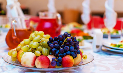 Wedding. Event. Banquet. Decorated festive table with plates and glasses, beautiful white napkins. A plate of grapes, apples and peaches. Decanters with Morse red.