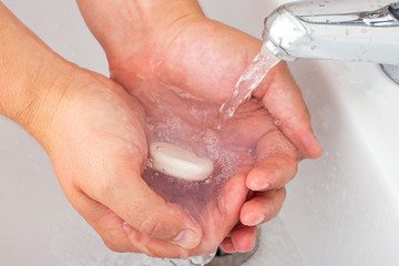 Fototapeta premium A man draws water in his hands with anti-bacterial soap in order to wash his face.