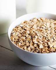 Rolled oats or oat flakes in bowl with bottle of milk on white background.