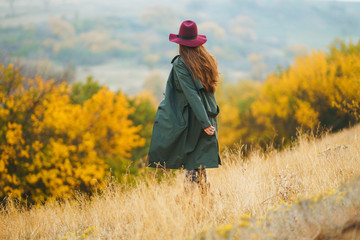 Beautiful young stylish girl in a coat walks in the autumn in the park. The girl is dressed in a green coat and a red hat. Beautiful evening. Autumn fashion. Lifestyle. High fashion portrait. 