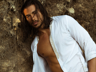 ragazzo con una camicia bianca aperta davanti alle rocce sembra seducente