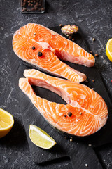 Two fresh raw salmon steaks with salt, peppers, lemon on stone background.