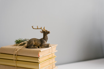 A stack of books in crane paper and a statuette of a sitting deer on a gray background. Copy space