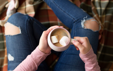 Girl sitting on a plaid and holding a cup of hot chocolate with marshmallow, top view