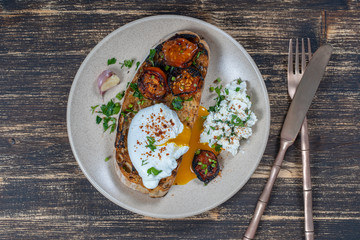 Poached egg on a piece of bread with fried red tomato, garlic and cottage cheese on a plate, close up
