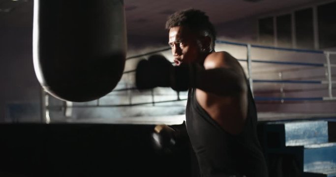 African american athlete is training in a gym, hitting a punching bag in boxing gloves, keeping fit before a fight - sports, active lifestyle concept 4k footage