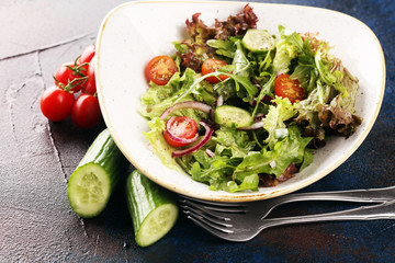 bowl of salad with vegetables and greens, with tomato, cucumber and onions on rustic table