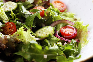 bowl of salad with vegetables and greens, with tomato, cucumber and onions on rustic table