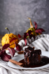 Small pumpkins in the background autumn scene indoor.Delicious chocolate cake on plate on table.Tasty chocolate cake. Piece of chocolate cake with warm fudge sauce, vertical