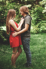 Fototapeta premium Vertical photo. happy married couple Husband hugs a beautiful adult pregnant wife. walks in a park. Second trimester. Holds his hands on her stomach. benefits of walking during pregnancy, 