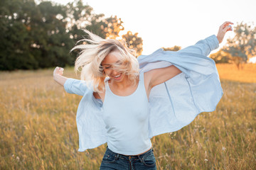 Obraz premium Happy young woman walking on the field at sunset.