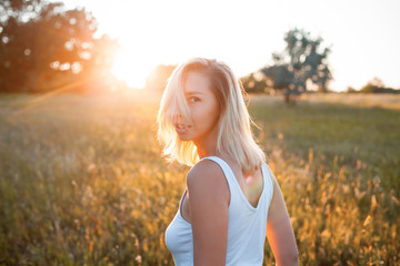 Fototapeta na wymiar Young woman in white shirt walking on the field at sunset. Back