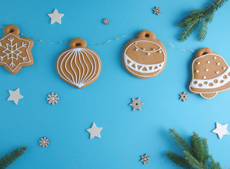 Tasty gingerbread cookies. Christmas toys hanging on a blue background on a garland - handmade gingerbread cookies. Against the background are wooden stars and snowflakes. 