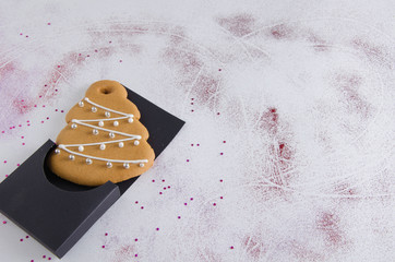 Christmas gingerbread - Christmas tree lies on a black packaging and on a white background. Against the background of shiny red glitter and sparkles-snowflakes.