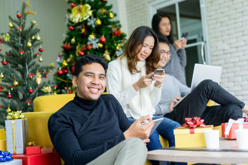happiness young handsome latin man smile with friends playing internet on device and laughing together in living room decorated with pine tree at house prepare for party merry christmas concept