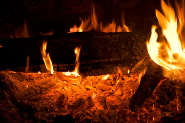 Close up of campfire at night showing logs, flames and burning embers.