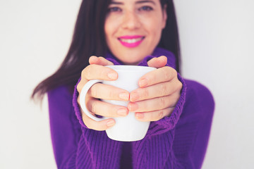 Close up of a beautiful young woman holding a cup of hot coffee in winter outfit at home