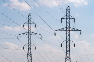 Two electricity poles and power lines against morning blue sky with white clouds. Energy supply.