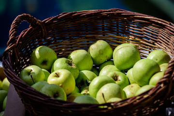 Group of fresh green apples in a wooden basket, available for sale at a street food market, natural background, soft focus