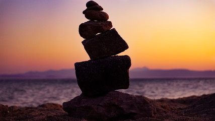 Fototapeta na wymiar Perfect balance of stack of rock stone tower at seaside towards beautiful outdoor evening sunset. Balance, harmony, meditation concept. Helping or supporting someone for growing or going higher up. 