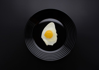 Fried egg on a stylish black plate. Breakfast. Awesome black background. Stylish design. Egg white and yolk. Top view. Organic food. Space for a text.