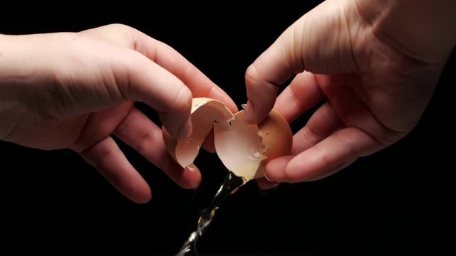 Female hands holding a cracked egg. Breaking an egg. Black background. Slow motion.