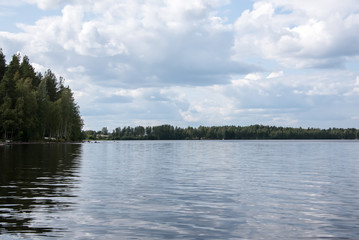 Summer view of the lake Hallanlahti with clouds on blue sky .