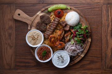 Mixed turkish kebab plate with rice, vegetables and dip sauces isolated on wooden background