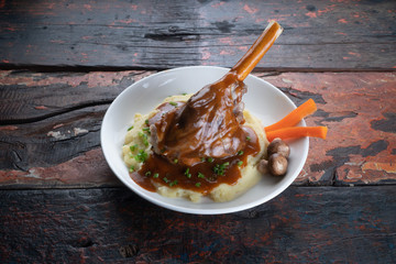 Turkish lamb shank in dark sauce with potato puree and vegetables isolated on rustic wooden table