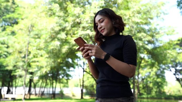 slow-motion of woman walking and using smartphone in park