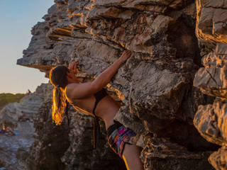 CLOSE UP: Muscular girl climbs a cliff by remote beach on sunny summer evening
