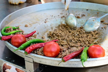 Traditional Turkish shaorma meat being prepared with red tomatoes and red and green peppers, available for sale at a street food market, selective focus