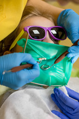 Dentist performing dental filling procedure to preteen girl in pediatric dental clinic. Doctor removing caries using high-speed dental drill. Calm child is sitting in a dental chair holding mouth open