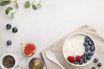 Obraz na płótnie Canvas natural healthy superfood fermented yogurt with blueberry, figs, chia seeds and raspberry in white bowl on light gray table. Image is copy space and top view