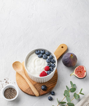 natural healthy superfood fermented yogurt with blueberry, figs, chia seeds and raspberry in white  bowl on light gray table. Image is copy space and top view