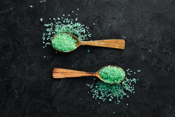 Green sea salt in a spoon. On a black stone background. Spa treatments.