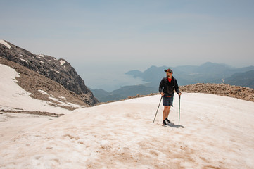 Young man standing on the dirty snow on the Tahtali mountain with hiking sticks